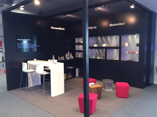 Messestand mit Einbauregalen, Br�ckentisch, Loungehocker, Beleuchtung
gefr�sten Logos und eingebautem Display